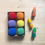 Eine Kartonbox mit 6 Häkelbällen von Kokomoo in rot, orange, gelb, grün, blau und grün. Daneben liegen drei kleine Holzzwerge von Grapat in orange, gelb und grün.