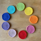 9 im Kreis aufgelegte, einfärbig bunte runde Häkeldecken in den Farben gelb, orange, pink, rot, rosa, lila, blau, türkisblau und apfelgrün.