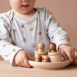 Ein Kind, das eine Holzschale in Händen hält. In der Schale sind kleine, bunte Holzkegel, die Grapat Nins und 3 Töpfchen aus Naturholz, die Grapat Mates.