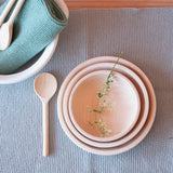 Ein Draufblick auf ein blaues Stricktuch. Darauf stehen ineinander 3 verschieden große Holzschalen mit einer Blüte darauf. Daneben liegt ein kleiner Kochlöffel für Kinder aus Holz.