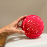 Eine Hand hält den rot-weiß gesprenkelten Mini-Stapelstein Confetti Red&Blush hoch.