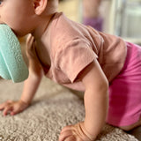 Krabbelndes Baby transportiert einen mintfarbenen Mini-Stapelstein mit dem Mund.