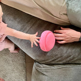 Ein rosafarbener Mini-Stapelstein, ein Baby greift danach, daneben liegt ein Erwachsener, nur die Hand ist zu sehen.