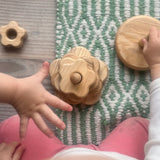 Man sieht einen Draufblick auf ein sitzendes Kind, das vor sich einen Steckturm aus Naturholz hat. Auf diesem Steckturm sind Blumenformen verschiedener Größen mit Loch auf einen Steckteil gestapelt.