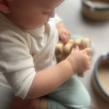 Seitenansicht eines kleinen Babies, das in der Hocke sitzend einen Steckturm aus Naturholzscheiben in Händen hält