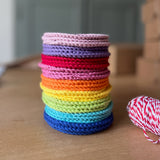 Ein Stapel bunter runder Häkeldeckchen in den Farben des Regenbogens stehen auf einer Holztischplatte.