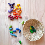 Die 36 Stück Grapat "Rainbow Snowflakes" Mandalasteine in Schneeflocken-Form liegen kunterbunt am Boden und in einem Korb.