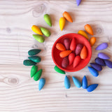 Grapat "Rainbow Snowflakes" Mandalasteine in Schneeflocken-Form liegen am Boden verstreut, bis auf alle roten Teile, die liegen in einer roten Holzschale.