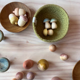 In einem grünen Köbchen liegen kleine Holzpilze, daneben in einer Holzschale liegen drei kleine Eicheln aus Holz, rundherum stehen weitere Spielfiguren von Grapat Moonlight Tale.