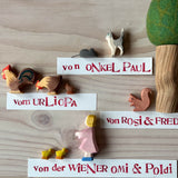 Ostheimer tierische Spielfiguren aus Holz: Katze, Maus, Hahn, Henne, Küken, Eichhörnchen, Figur Tochter. Neben dem Eichhörnchen ist ein Filzbaum mit grüner, runder Krone. Daneben liegen Namensschilder, die erklären, wer die Figuren geschenkt hat, zum Beispiel "von Onkel Paul".