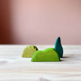 Verschieden große Holzstücke in Grüntönen stehen versetzt hintereinander, dass sind die Gebüsche von Ostheimer, beliebte Spielfiguren aus Holz für Kinder zum Spielen.