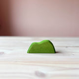Mittelgrünes stehendes Holzstück mit zwei Wellen an der Oberkante, ca. 5cm hoch. Das ist das mittelgrüne Gebüsch von Ostheimer, eine beliebte Holzfigur zum Spielen für Kinder.