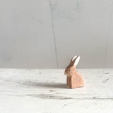 Die Ostheimer Spielfigur "Hase sitzend" sitzt auf einer Holzplatte und schaut nach links. Die natürliche braune Farbe ist gut zu sehen.