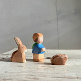 Drei holzspielfiguren von Ostheimer stehen nebeneinander mit Blick nach rechts. Ein Hase mit stehenden Ohren, ein kleiner Zwerg mit Rucksack und Kappe und ein kleines Häschen.