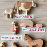 Die Ostheimer Spielfiguren Kuh, Kalb, Heidi, Schwein, Ferkel und Pferde sind zu sehen. Dazwischen liegen Namensschilder, die zeigen von wem die Figuren geschenkt wurden, zum Beispiel "von Oma und Opa".