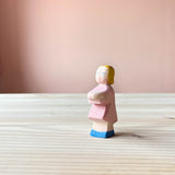 Die Ostheimer Spielfigur Tochter handbemalt steht auf einer Holzplatte und schaut nach vorne.