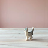 Eine Spielfigur aus Holz, nämlich eine grau-weiße Katze steht auf einer Holzplatte und schaut nach links.