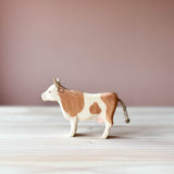 Ostheimer Kuh Spielfigur für Kinder aus Holz mit braunen Flecken, steht mit erhobenem Kopf und Blick nach links.