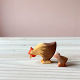 Zwei Spielfiguren aus Holz sind zu sehen: Ostheimer Huhn und ein braunes Küken. Das Huhn pickt scheinbar Futter, das Küken steht hinter der Henne.