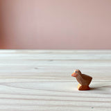 Die Ostheimer Küken Holzfigur zum Spielen ist braun, steht auf einer Holzplatte und schaut nach links.