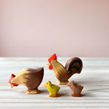 Vier Spielfiguren aus Holz sind zu sehen: Ostheimer Hahn, Henne und ein gelbes und ein braunes Küken. Hahn und Küken stehen, das Huhn pickt scheinbar Futter.