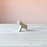 Das weiße laufende Lamm von Ostheimer steht auf einem hellen Holzuntergrund und ist seitlich ausgerichtet.