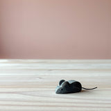 Eine kleine dunkelgraue Ostheimer Spielfigur Maus aus Holz, liegt auf einer Holzplatte und schaut nach links.