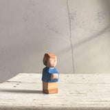 Ein Holzzwerg von Ostheimer, mit blauem Oberteil, brauner Hose und brauner Kappe steht auf einer Holzfläche und schaut nach vorne.