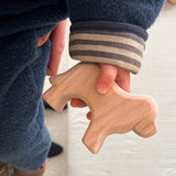 Man sieht den Arm eines Babies. In seiner Hand hält es einen Hund aus Naturholz.