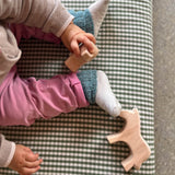 Ein Blick von oben auf ein sitzendes Baby. Es hat ein Holztier in einer Hand. Auf der karierten Matte liegt neben dem Fuß des Babies noch ein Holzpferd ohne Bemalung.