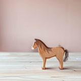 Eine Holzfigur zum Spielen, das Ostheimer Pferd braun mit Baumwollschweif stehend, mit Blick nach links.