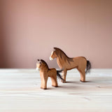 Zwei beliebte Spielfiguren von Ostheimer: Pferd braun mit Baumwollschweif und Ostheimer Fohlen braun mit Baumwollschweif stehen versetzt hintereinander.