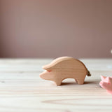 Eine Ostheimer Spielfigur aus Holz, das Schwein in rosa steht auf einer Holzplatte und schaut nach links. Am rechten Bildrand sieht man ebenfalls einen Schweinerüssel.
