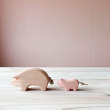 Eine Ostheimer Spielfigur aus Holz, das Schwein in rosa steht auf einer Holzplatte und schaut nach links. Dahinter steht das rosa Ferkel.