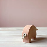 Eine Ostheimer Spielfigur aus Holz, das Schwein in rosa steht auf einer Holzplatte. Man sieht es von hinten, das Ringelschwänzchen ist aus einem kleinen Seil geknotet.