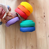 6 Stapelsteine® Classic in Regenbogenfarben und ein Confetti Classic Stein auf einem Holzboden.