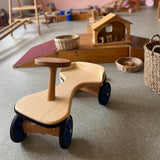 Das hochwertige Rutschauto aus Holz für Kinder ab 1 Jahr von Lautenbach steht vor einem Pikler Podest mit Holzstall darauf.