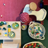 Das Holz-Rutschauto von Lautenbach für Kinder parkt neben Körben gefüllt mit Spielmaterial für freies Spielen nach Pikler.