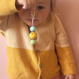 Ein Kind, das einen gelb-blauen Grapat Snowbuddy Christbaumanhänger in der Hand hält, der leicht baumelt.