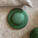 Blick von oben. Ein Stapelstein Balance Board in Dunkelgrün liegt mit der Unterseite nach oben auf einem grauen Teppich.