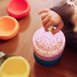 Eine Kinderhand legt einen Glitzerstern auf den obersten Mini Stapelstein im weihnachtlichen Confetti Design.