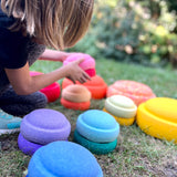 Ein Kind stapelt Stapelsteine Mini, die rings um es in verschiedenen Größen und Farben verteilt in der Wiese liegen.