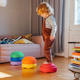 Ein Stapelstein Bundle Classic in Regenbogenfarben in drei verschiedenen Teilen, mal drei, mal zwei gestapelt, mal ein loser Stein. Ein Kind balanciert darüber.