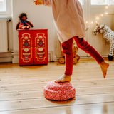 Ein Kind steht auf einem Bein balancierend auf dem rot weiß gemusterten Confetti-Stapelstein Red & Blush.