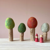 Vier Filzbäume für das Kleine Welt Spiel von Papoose Toys. Set mit vier Bäumen mit Holzstamm für alle vier Jahreszeiten, davor zwei Grapat Nins in Rot.