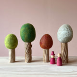 Vier Filzbäume für das Kleine Welt Spiel von Papoose Toys. Set mit vier Bäumen mit Holzstamm für alle vier Jahreszeiten, davor zwei Grapat Nins.