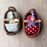 Die beiden Wichtelnest Puppenbettchen in rot und lichtblau nebeneinander gestellt. Links schläft ein weißer Nanchen Wichtel, rechts im roten Bettchen der lila Wichtel.