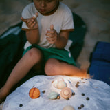 Ein Kind hält einen kleinen Mond von Grapat Dear Universe, vor ihm liegen weitere Planeten auf einem Tuch.