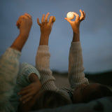 Kind liegen im Sand, es ist Nach, sie halten die Planeten von Grapat Dear Universe hoch in die Luft, die von einem Licht angestrahlt werden.