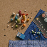 Das Spielset Grapat Dear Universe und anderes Spielmaterial aus Holz liegen am Strand oder Decken verteilt.